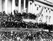 A large crowd in front of a large building with many pillars.