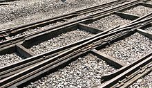 Three rails cross the picture from left to right supported on thick timbers; occasional smaller timbers cross between these and stone chippings fill the space between them.