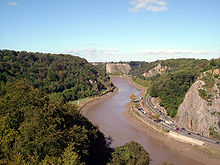 River flowing through gorge with wooded sides. On the right hand bank is a road.