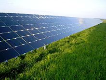 Solar panels, angled at about 30 degrees, reflect the blue sky from above a grassy field.