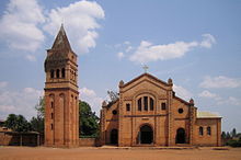 Photograph depicting the Catholic parish church in Rwamagana, Eastern Province, including the main entrance, façade, the separate bell tower, and dirt forecourt