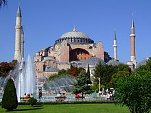 A reddish building topped by a large dome and surrounded by smaller domes and four towers