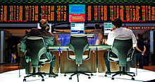 Two men sit at computer monitors with financial information