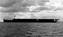 Aircraft carrier on the sea with cloudy sky in the background.